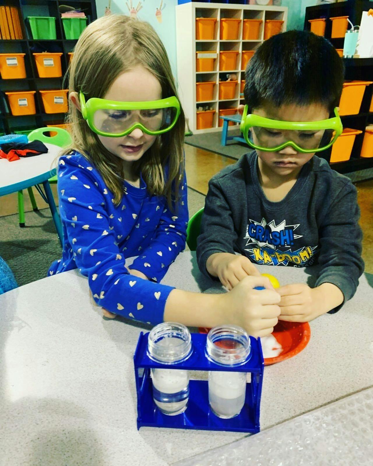 Two children wearing safety goggles doing an experiment in a classroom