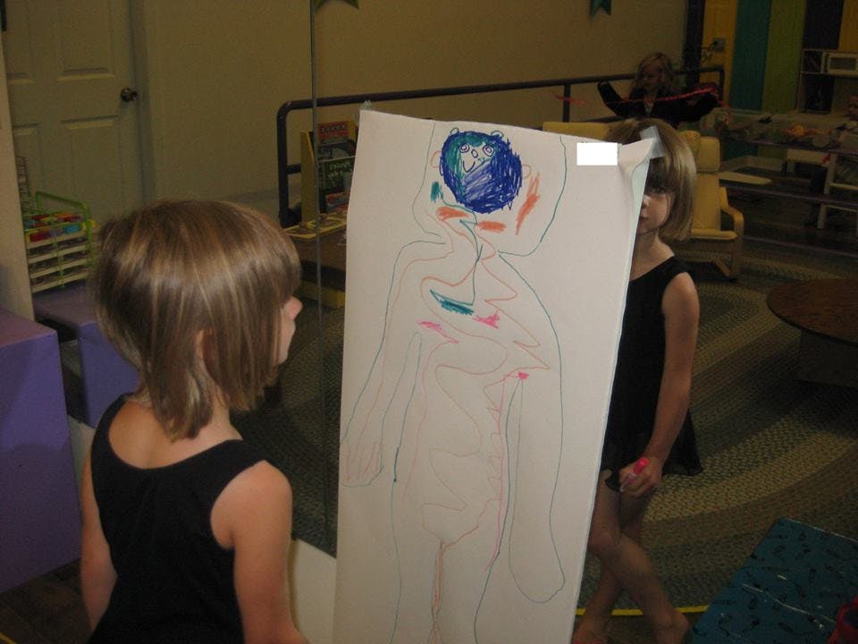 Child looking at a large drawing of a person, another child partially visible