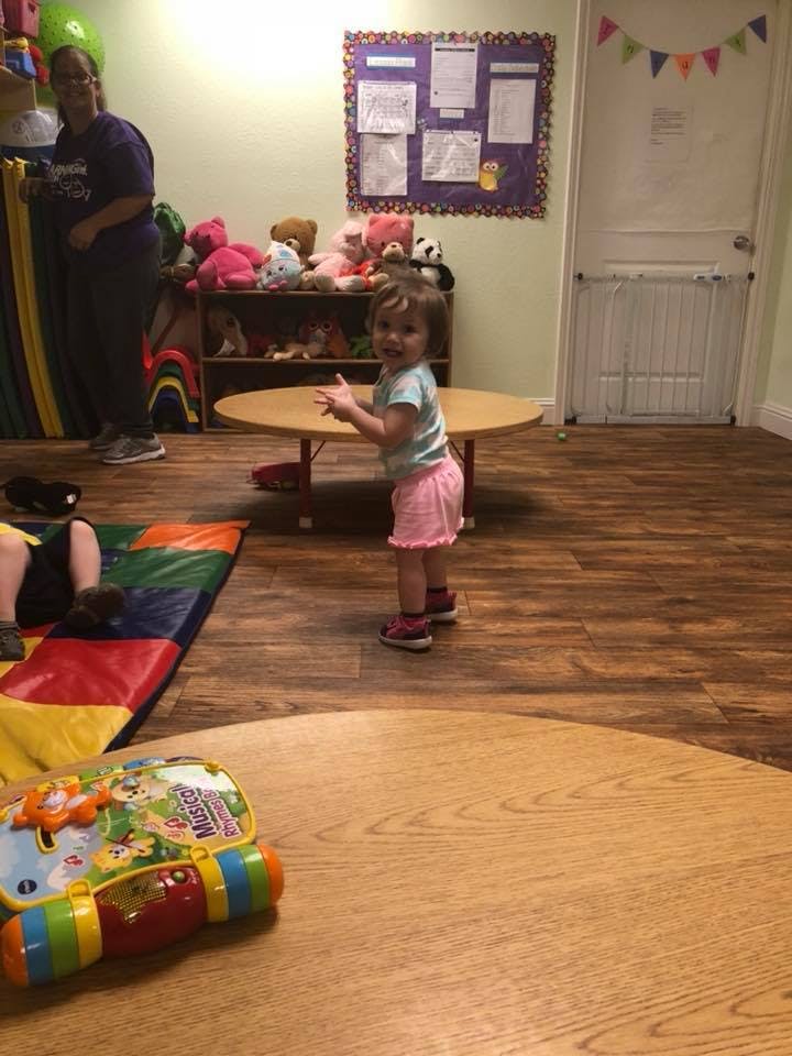 Child standing by a table in a room with a person in the background