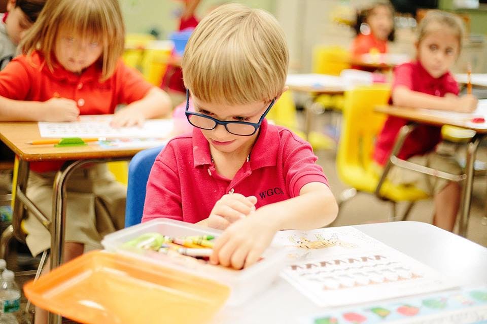 Child in glasses working at a desk in a classroom