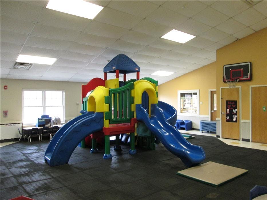 Colorful indoor playground structure with slides and a basketball hoop in a classroom