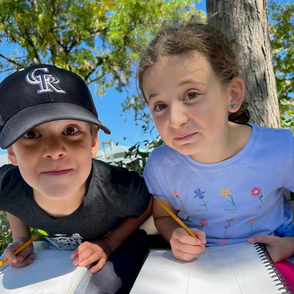 Two children drawing in sketchbooks outdoors