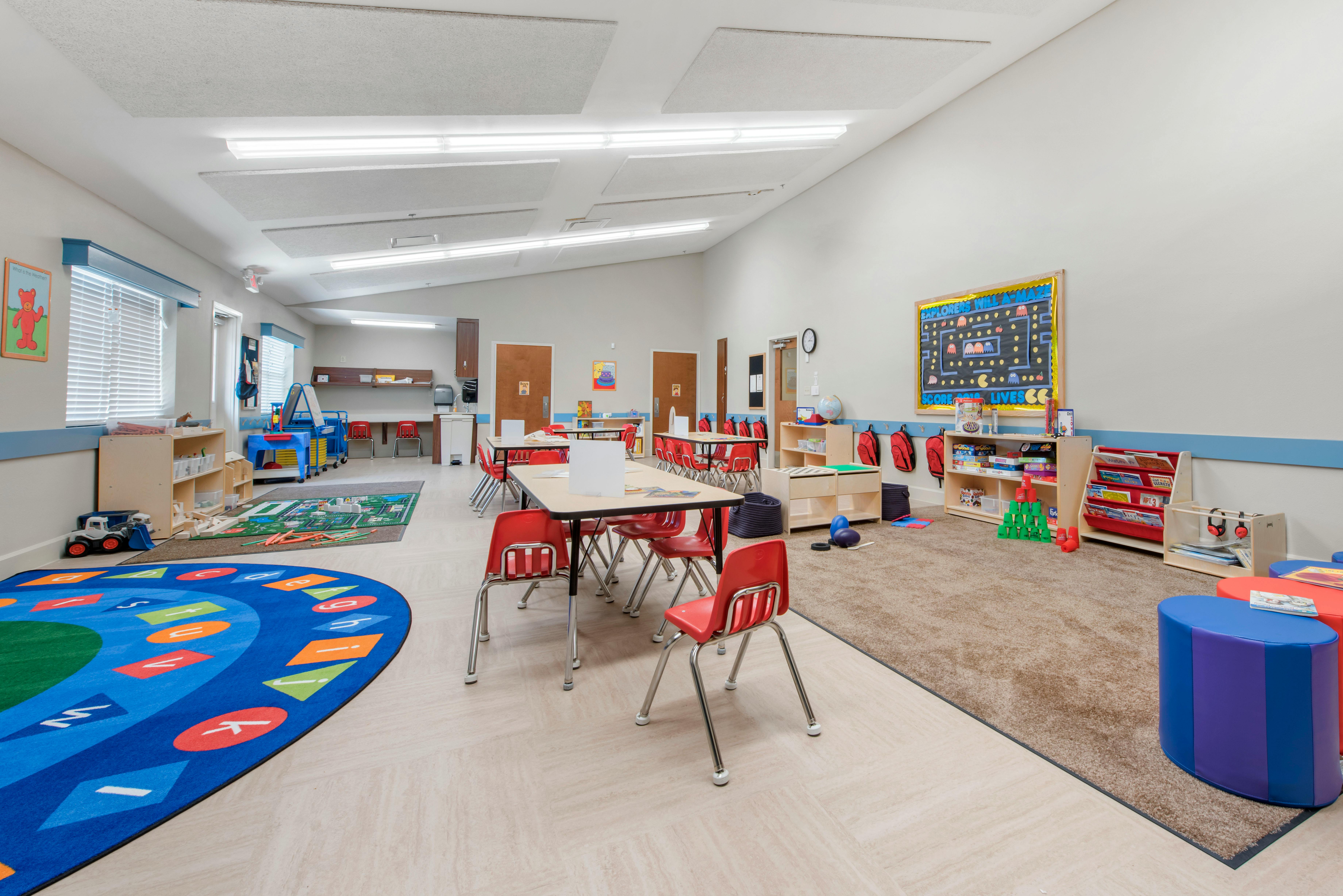 Empty classroom with small tables and chairs, play mats, and learning materials