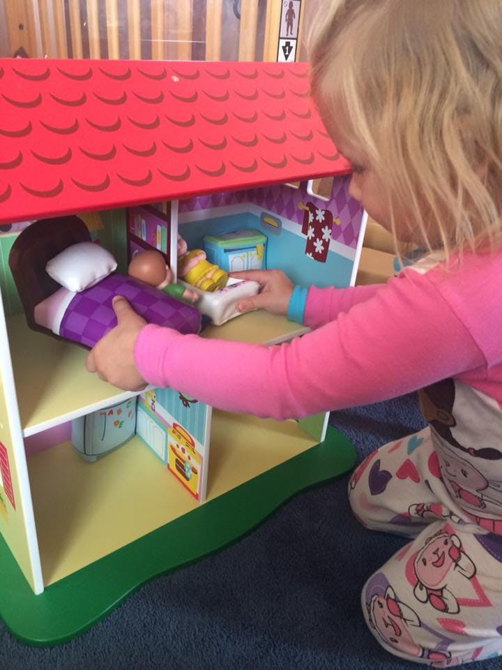 Child playing with a dollhouse, placing a doll in a bed