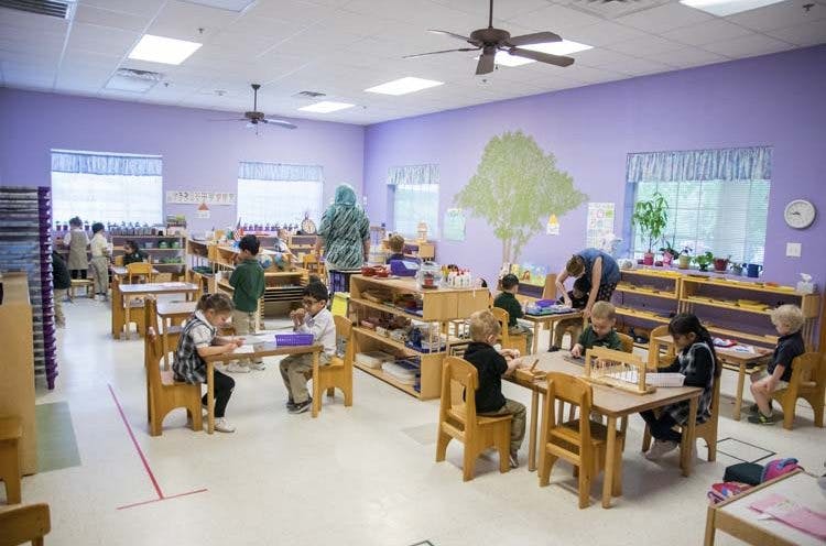 Children and adults in a classroom with tables and shelves