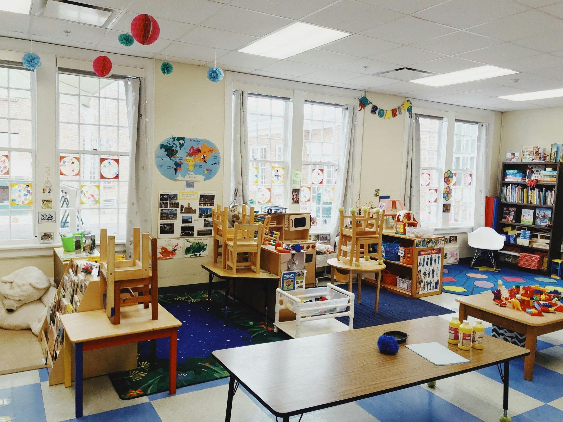 Classroom with small tables and chairs, a world map, and bookshelves