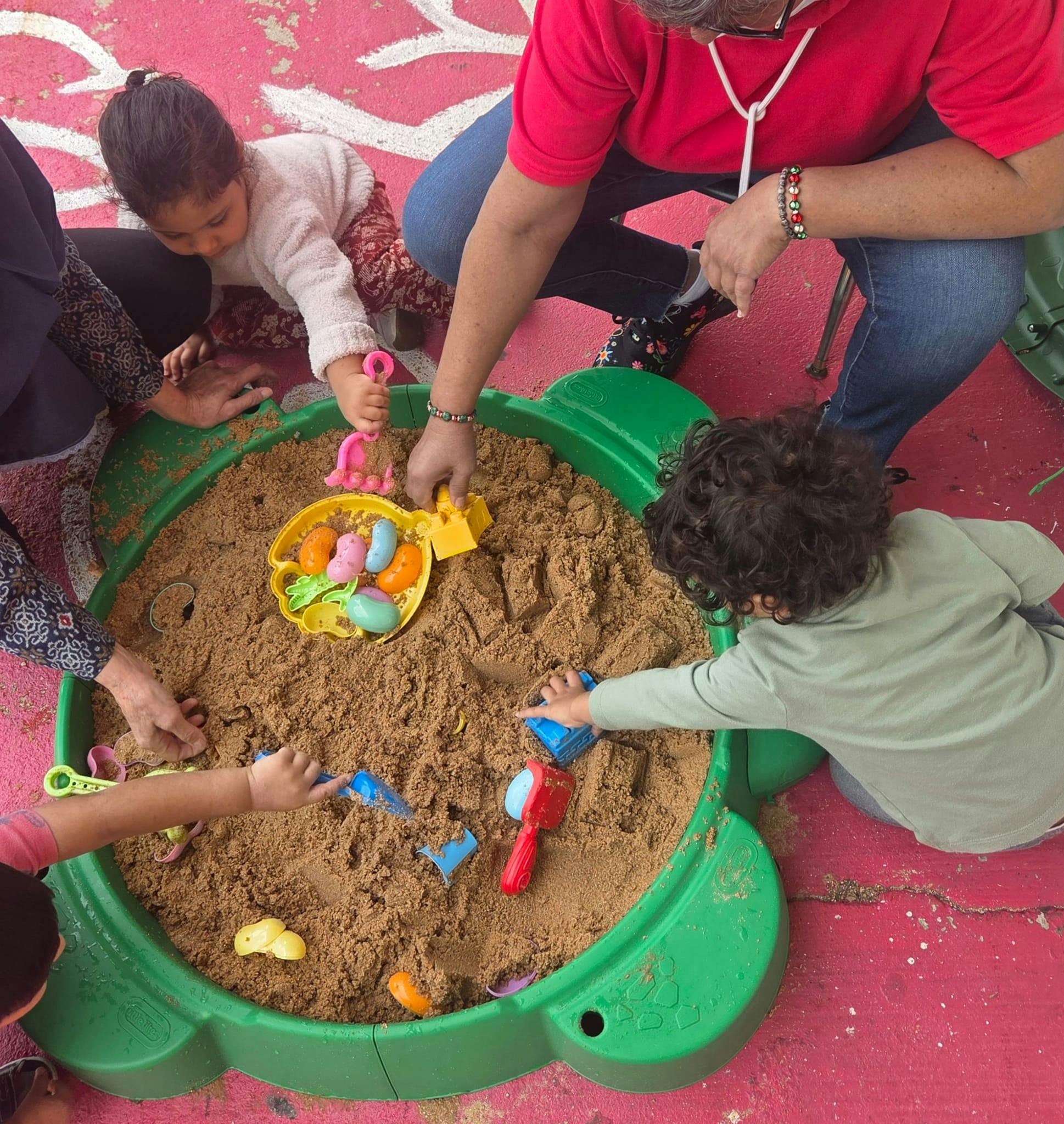 Adults and children playing in a sandbox with colorful toys