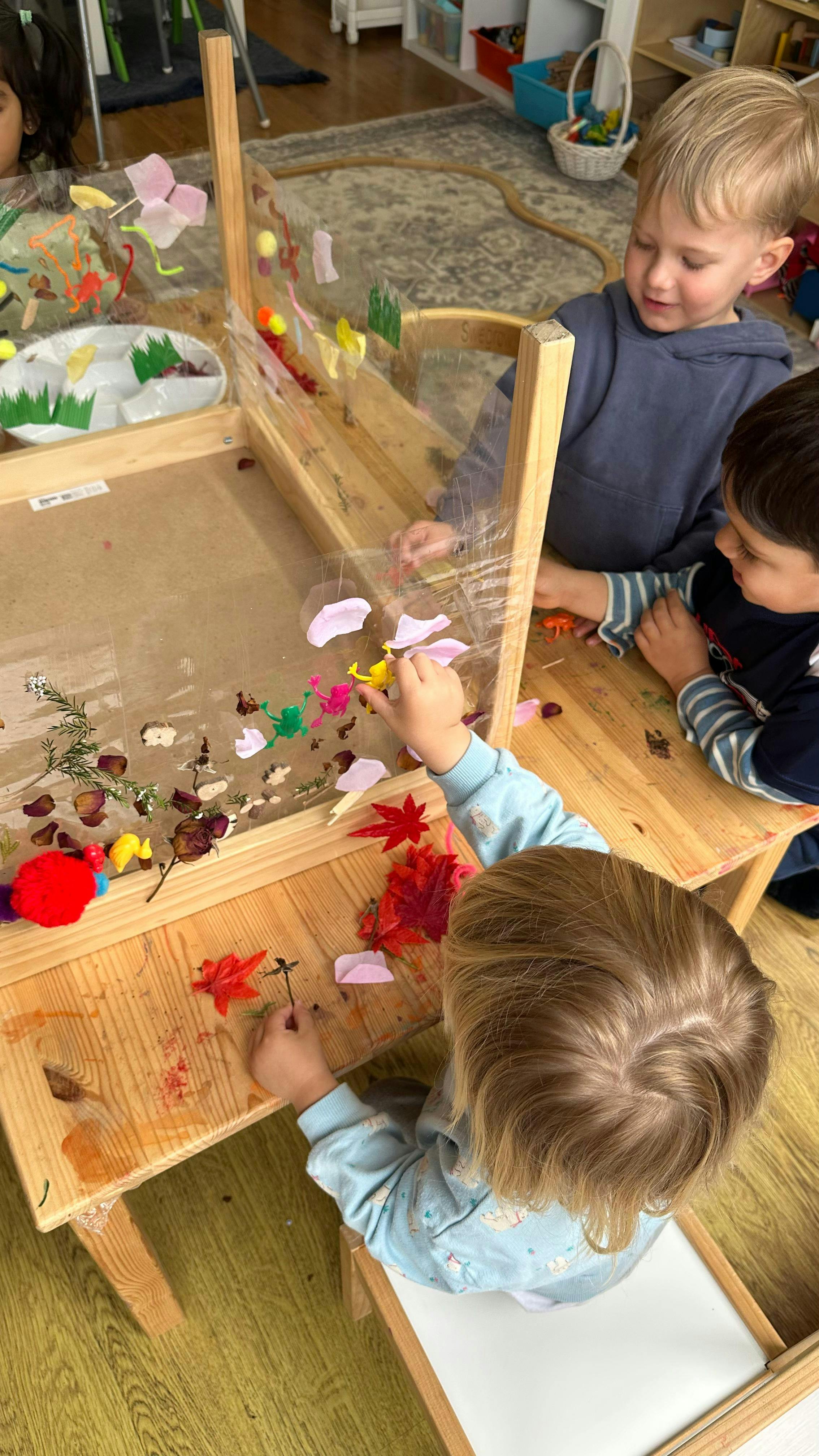 Children playing with natural elements and toys on a clear art easel
