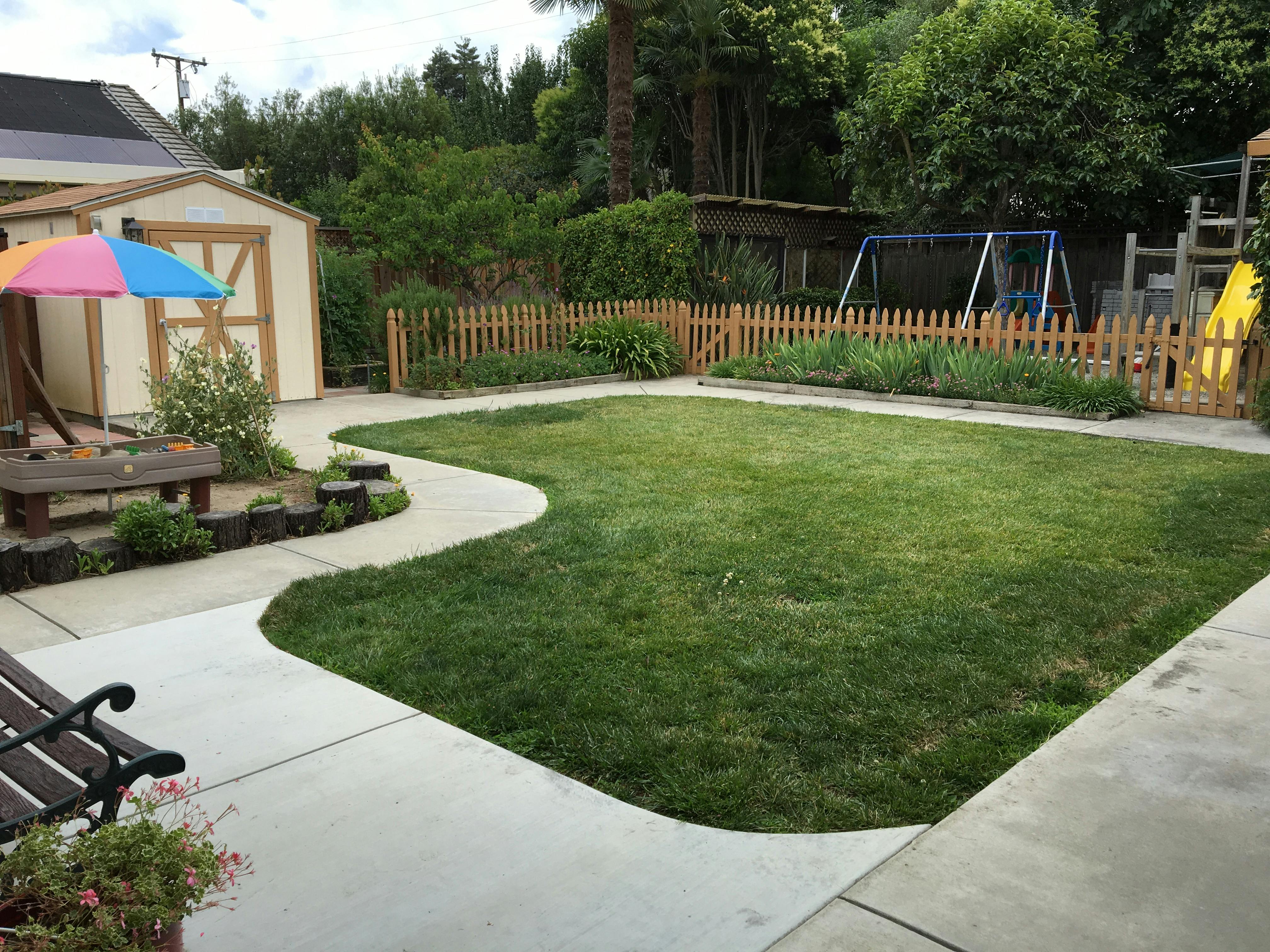 Backyard with a shed, green lawn, and a swing set behind a picket fence