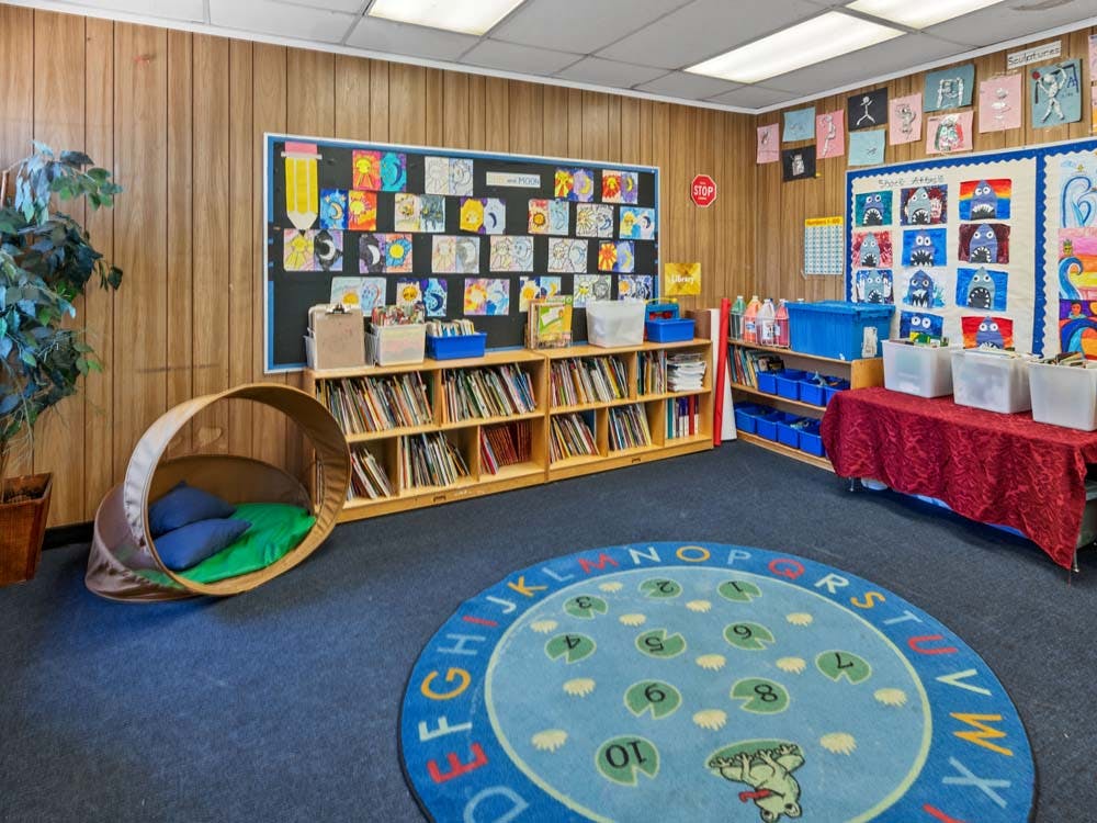 Classroom with child-level bookshelves, a round rug with letters and numbers, and a reading nook
