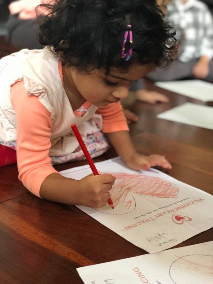 Child drawing on paper with a red colored pencil