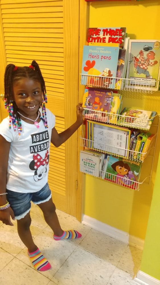 Child standing next to a wall-mounted book rack