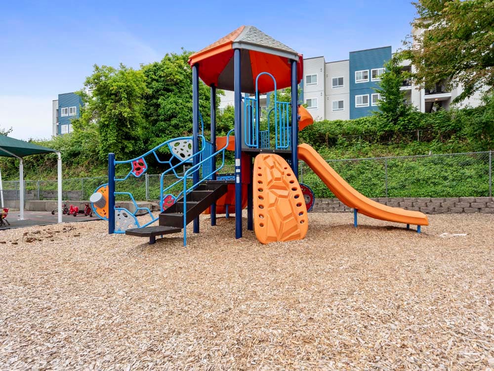 A colorful playground with an orange slide and steps on wood chips
