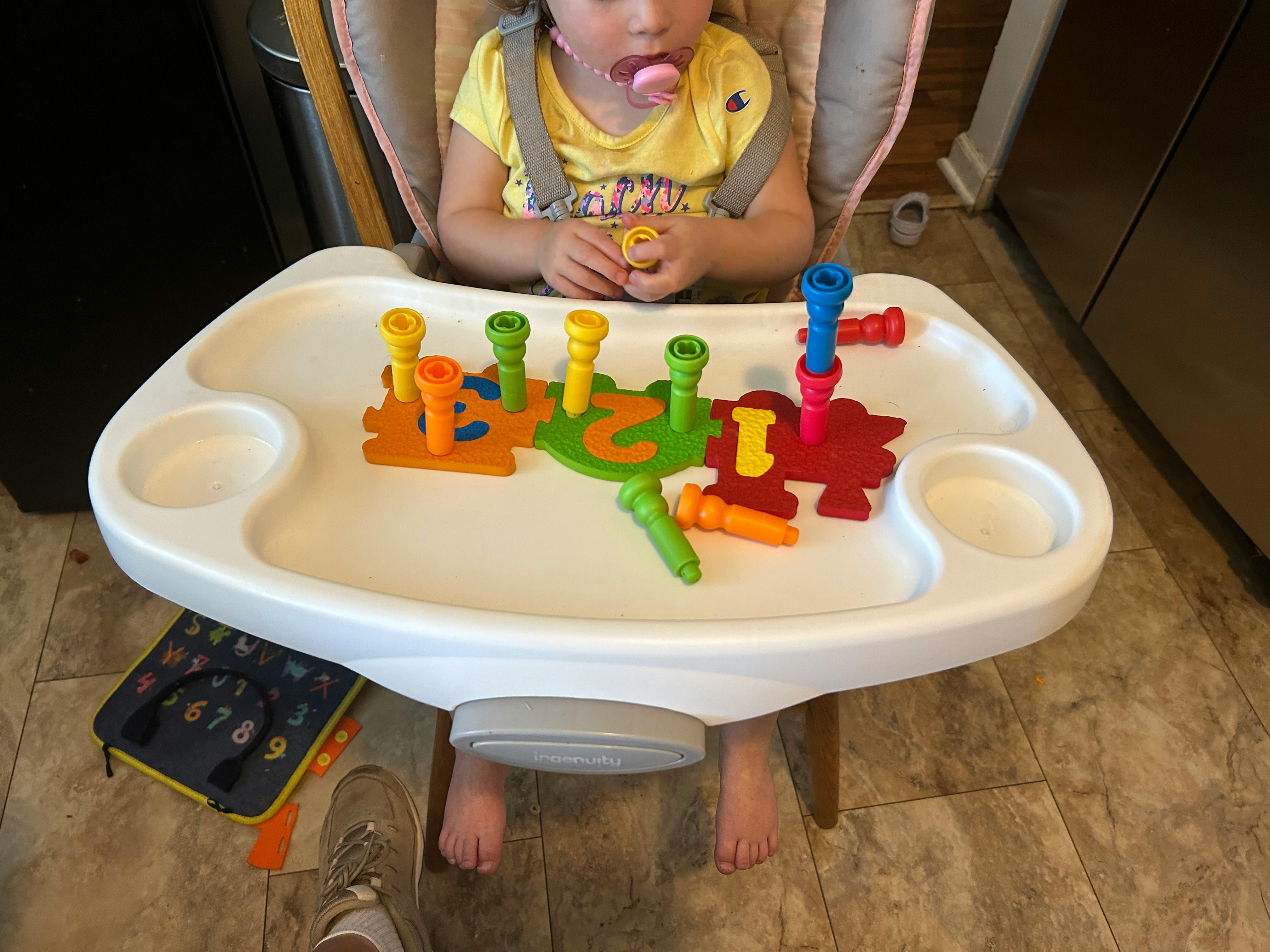Child in a high chair playing with colorful peg toys