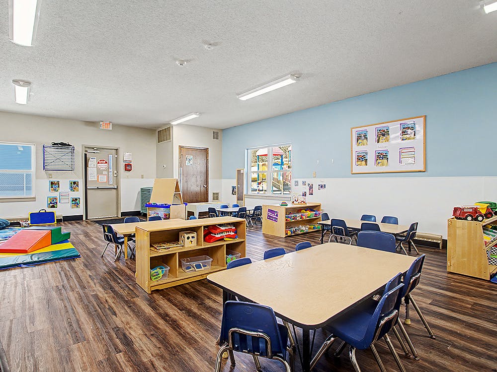 Empty classroom with tables, chairs, and shelves of toys