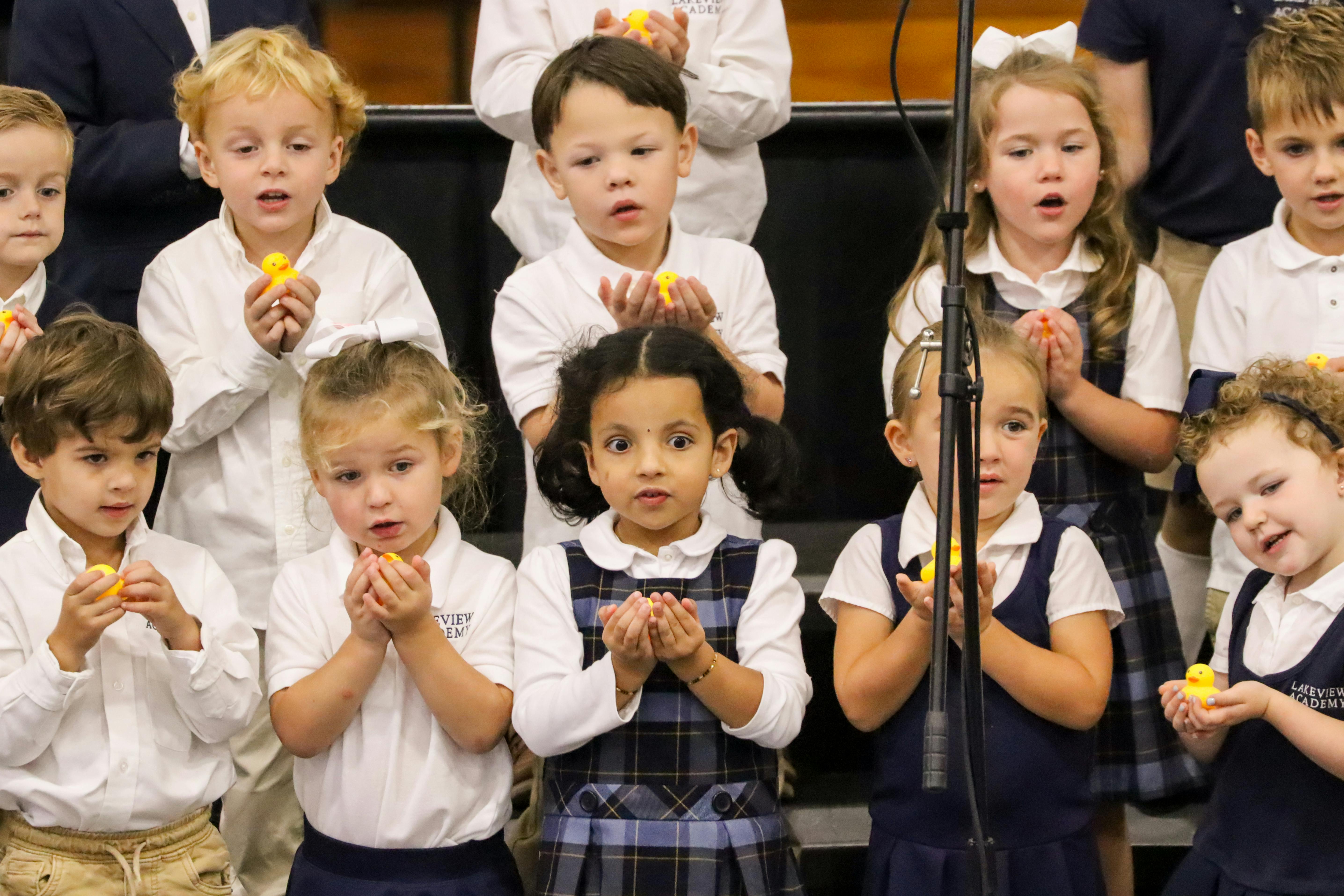 Group of children singing, some holding small yellow objects