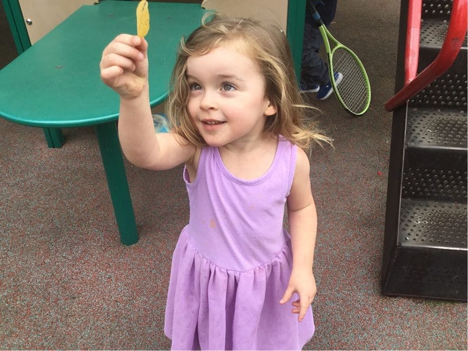 Child in a purple dress holding up a small yellow object
