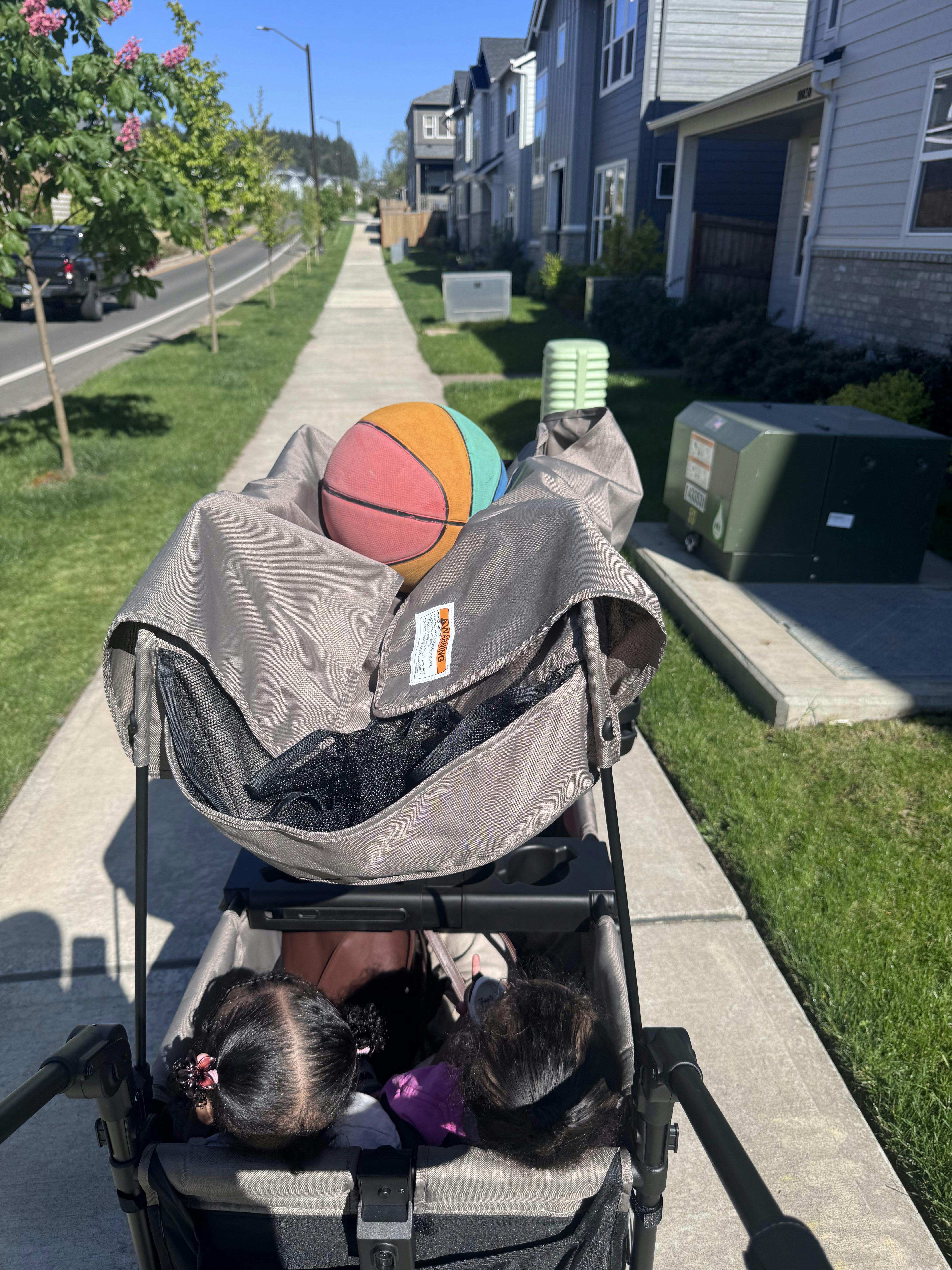 Basketball resting in a stroller pushed along a residential sidewalk