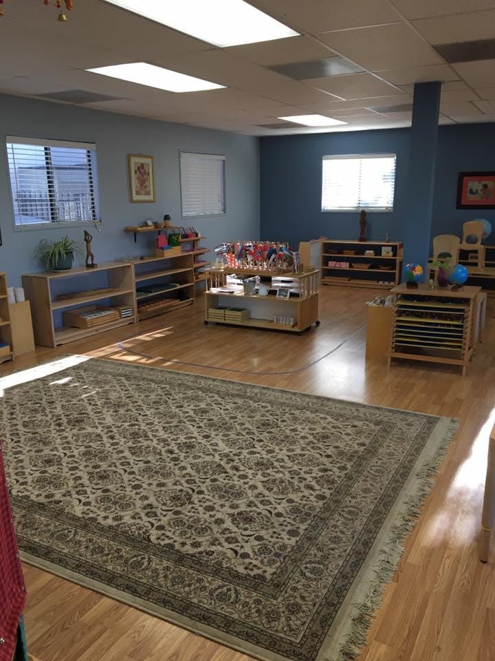 Classroom with wooden shelves and a large patterned rug on a wooden floor