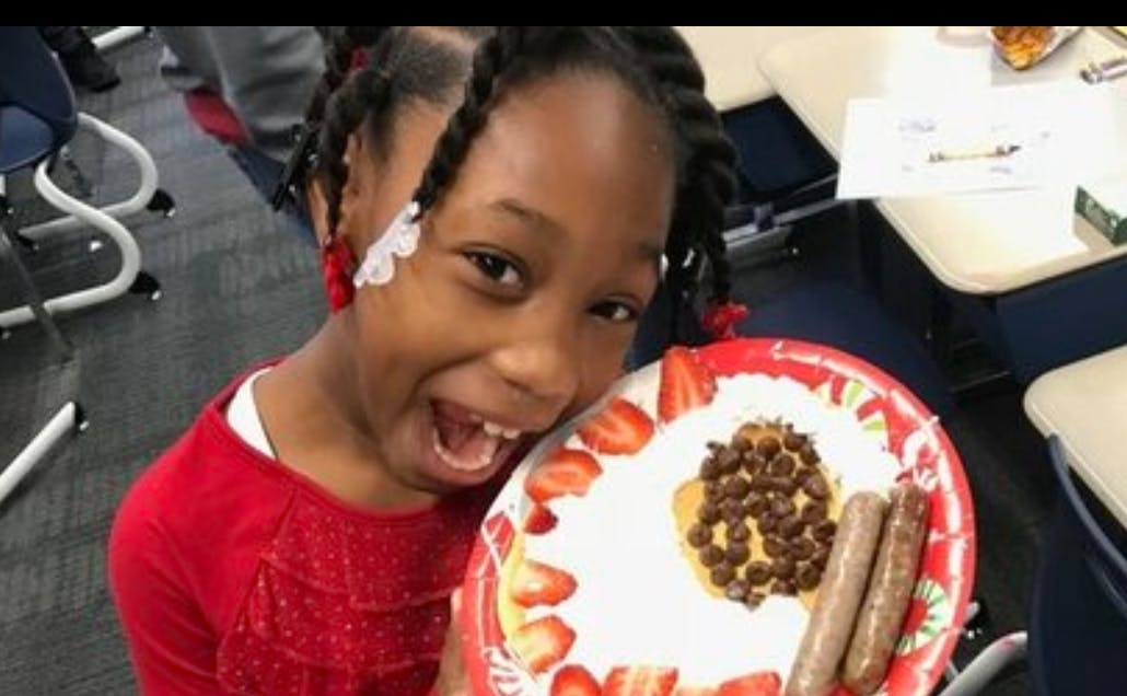 Child holding a plate with pancakes, strawberries, and sausage