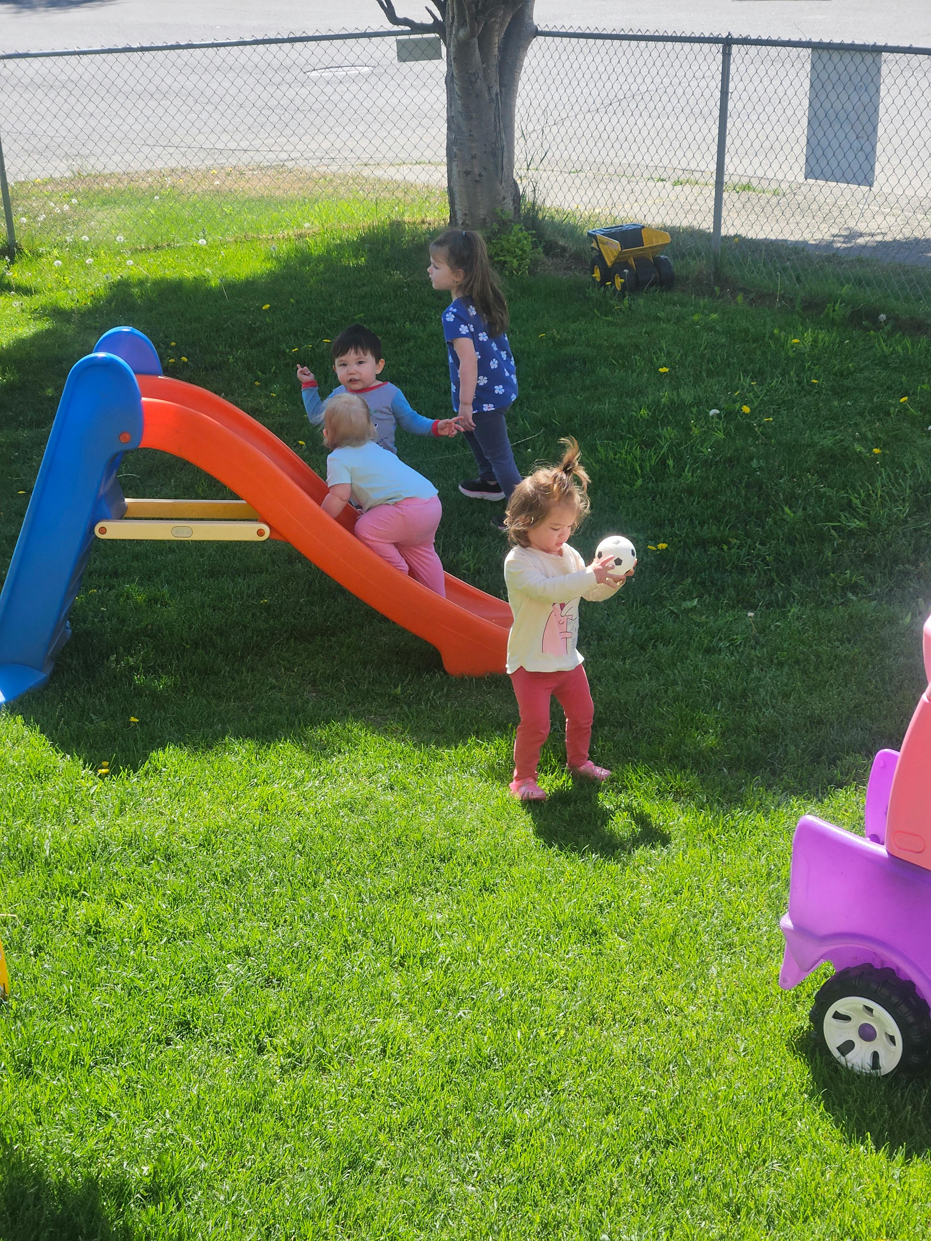 Children playing on a slide in a grass yard