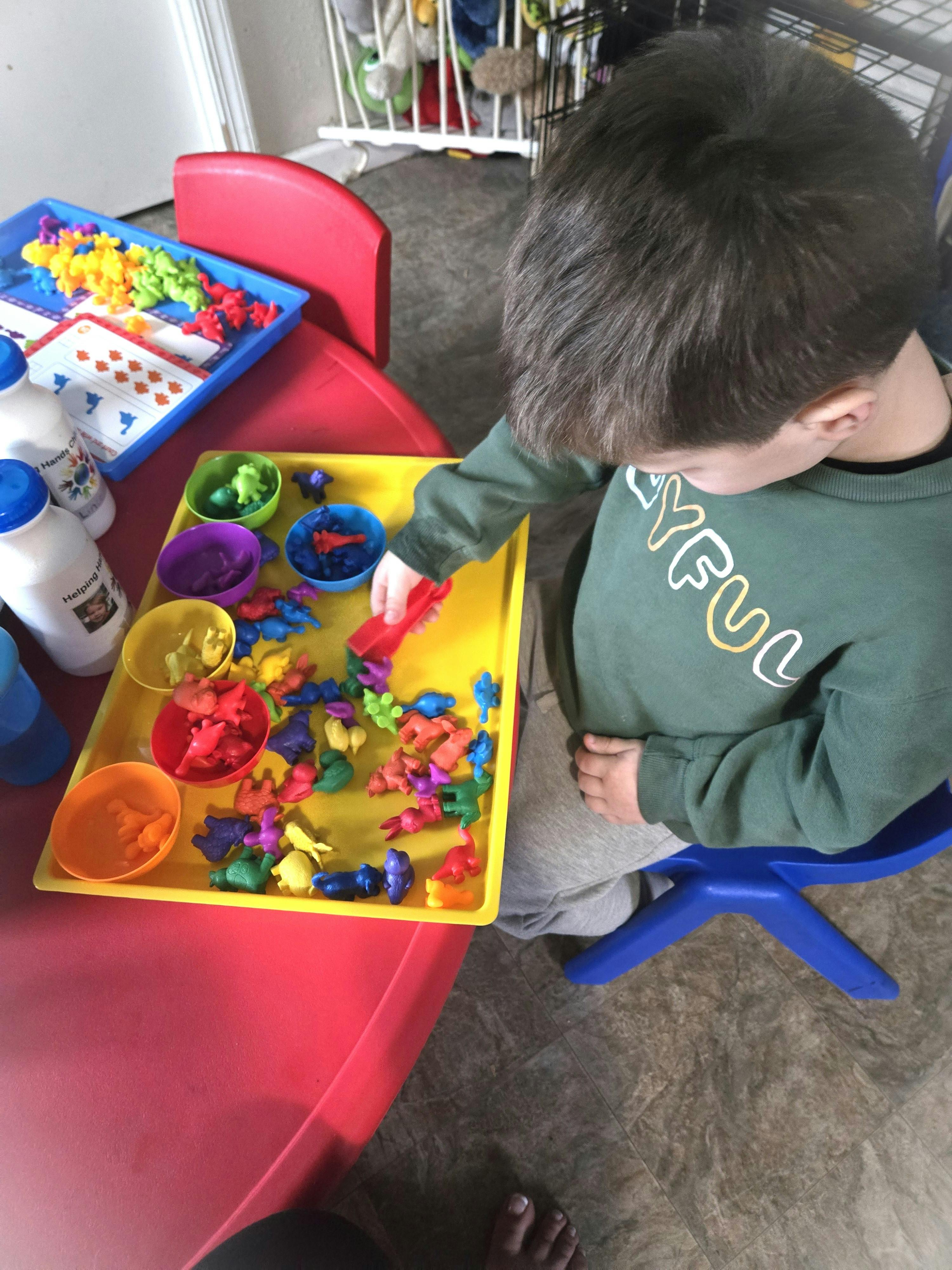 Child playing with small colorful animal figures on a tray