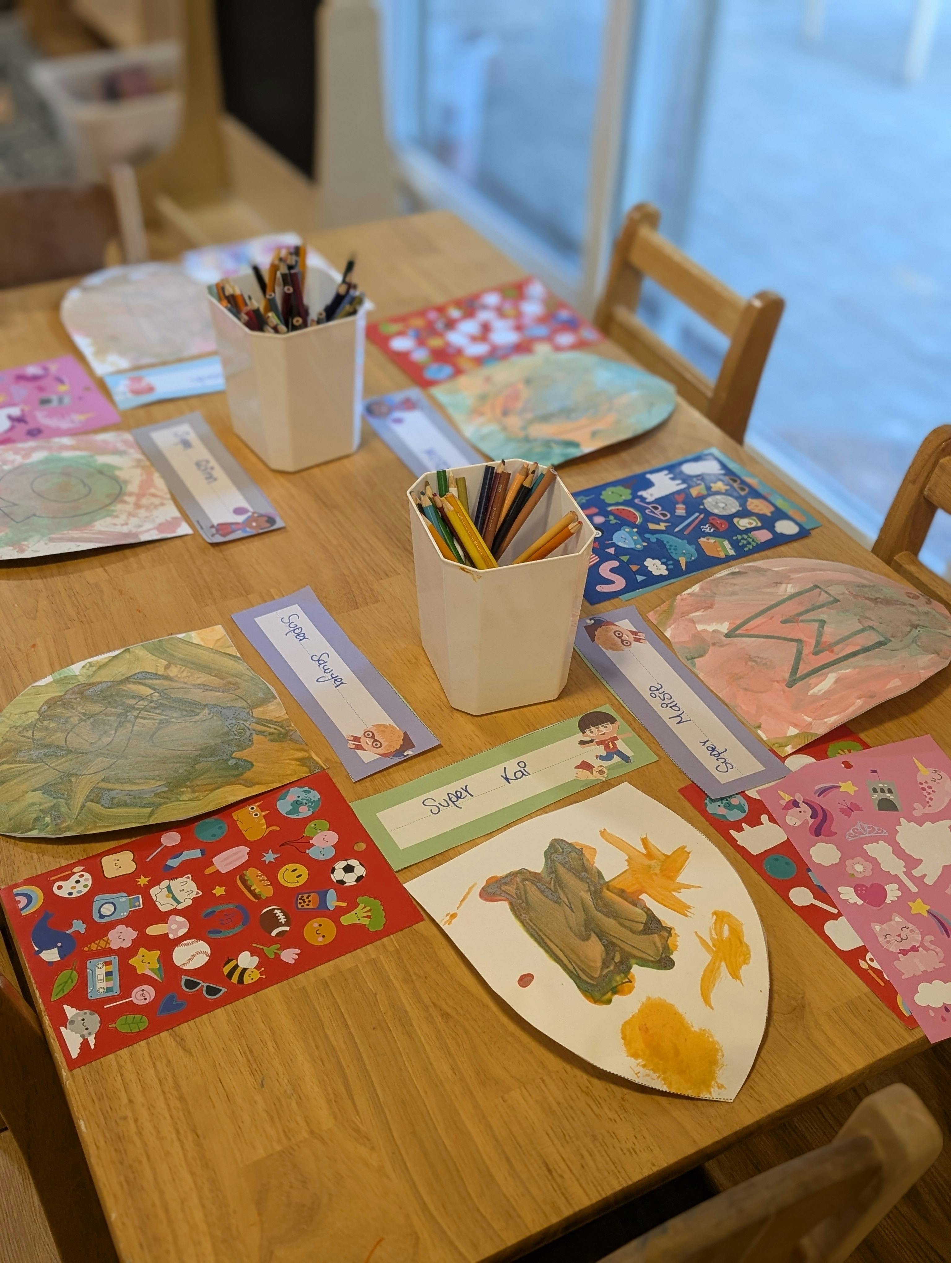 Craft supplies and artwork with name tags on a wooden table