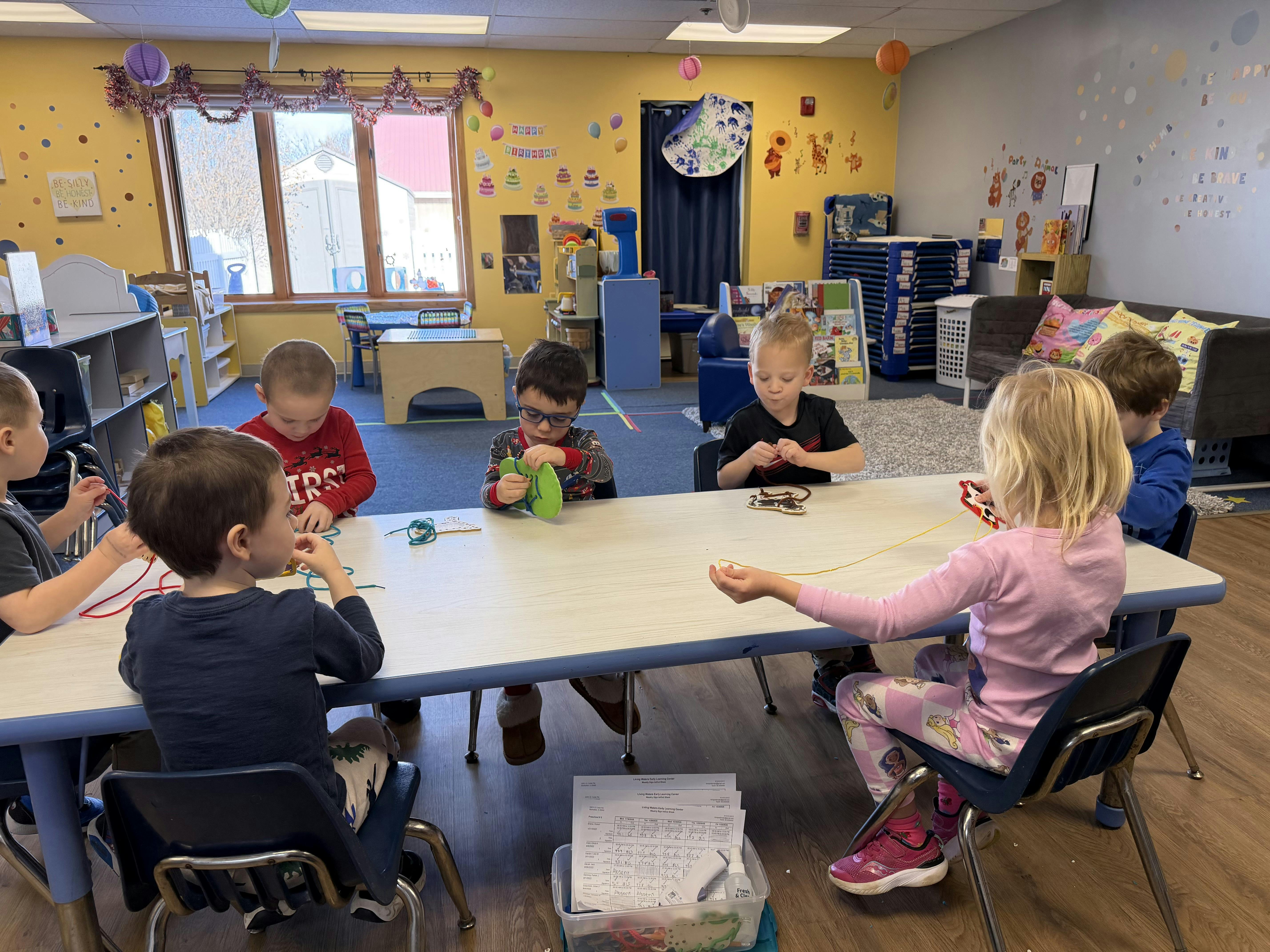 Children sitting at a table engaged in a lacing activity in a classroom