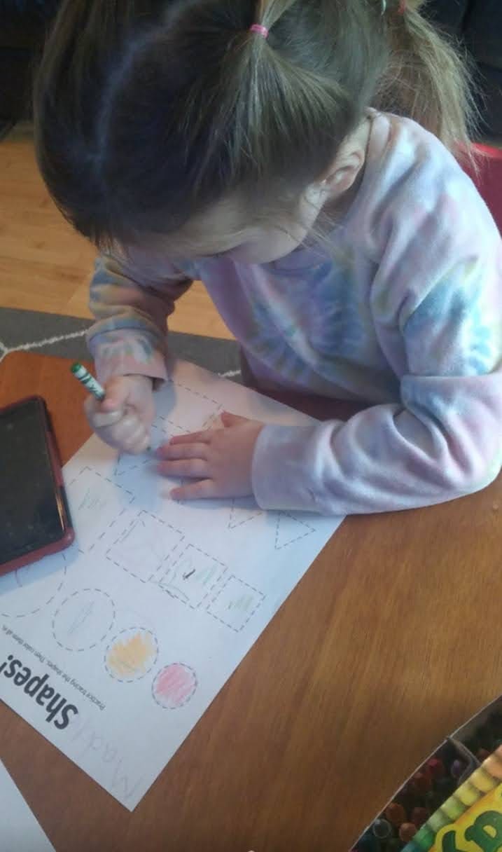 Child coloring a worksheet with shapes