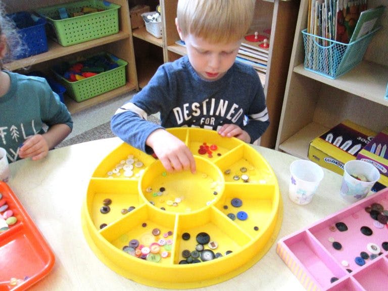 Child sorting small items in a yellow tray