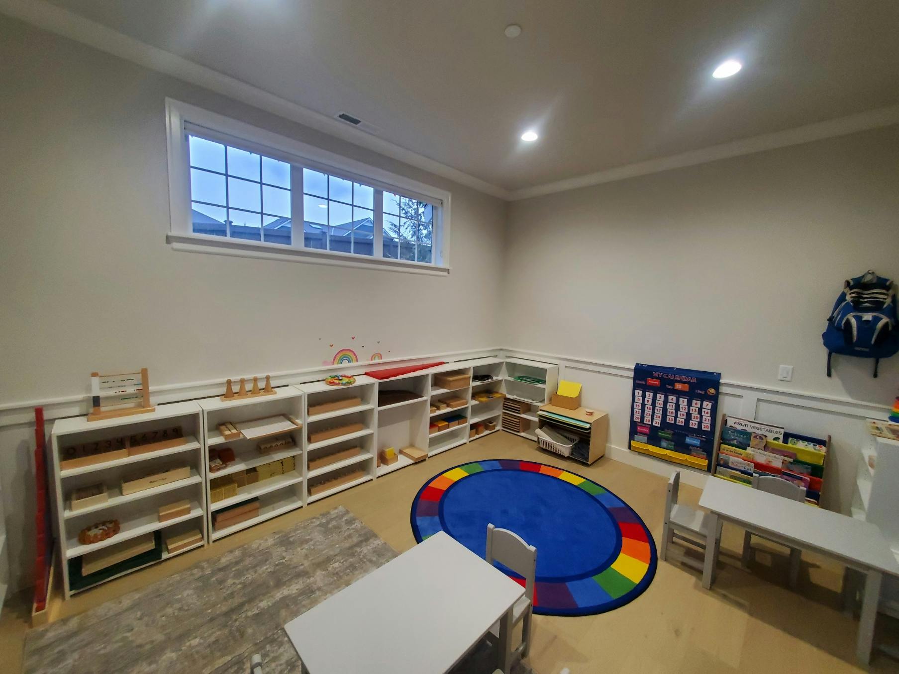 Classroom with shelves of learning materials, a colorful rug, and small tables