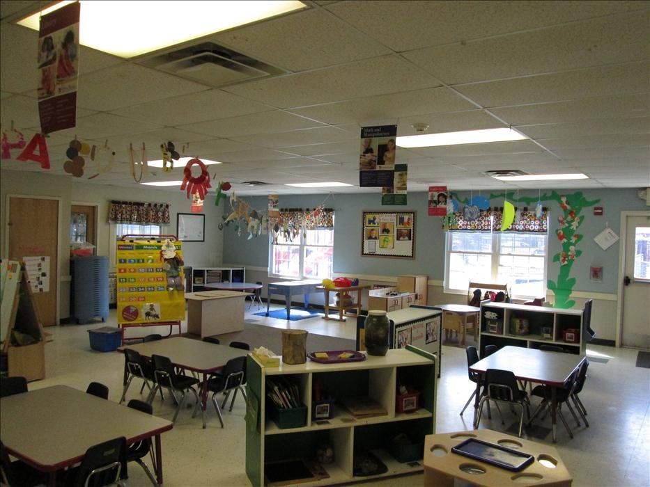 An empty classroom with small tables and chairs, and decorations on the walls