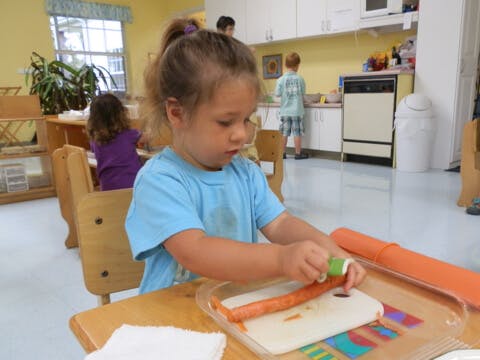 Child at a table spreading something on a food item in a classroom