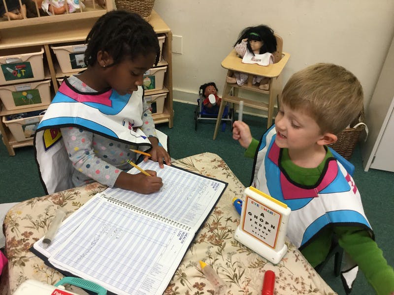 Two children in smocks writing and playing at a table