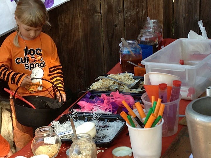 Child in orange shirt holding a black cauldron next to a table of craft supplies