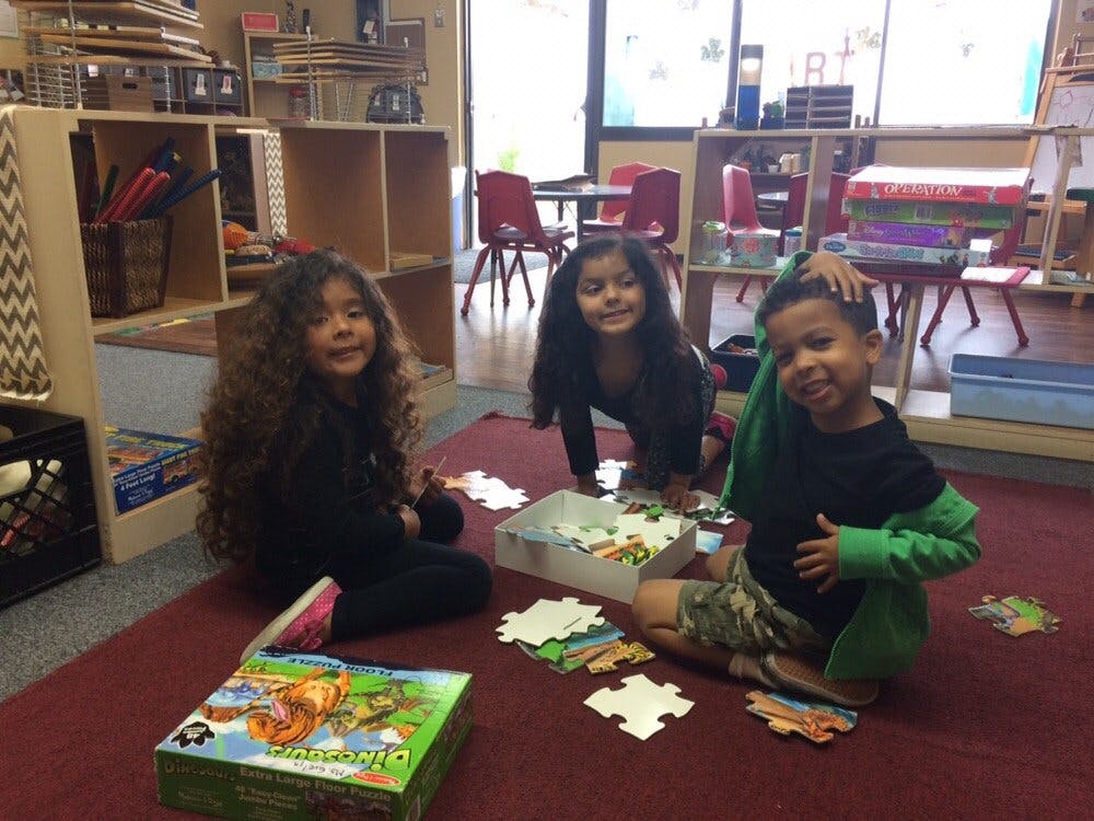 Three children playing with puzzles on a classroom floor