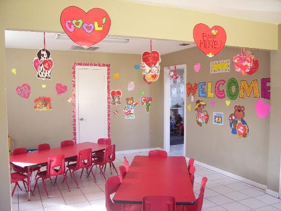 Classroom with red tables and chairs, decorated with hearts and a "WELCOME" sign