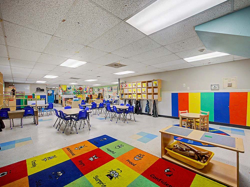 Colorful classroom with small tables and chairs, a play rug, and storage shelves