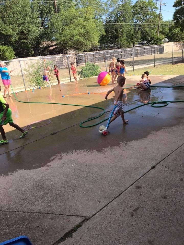 Children playing with water and a beach ball on a wet concrete surface