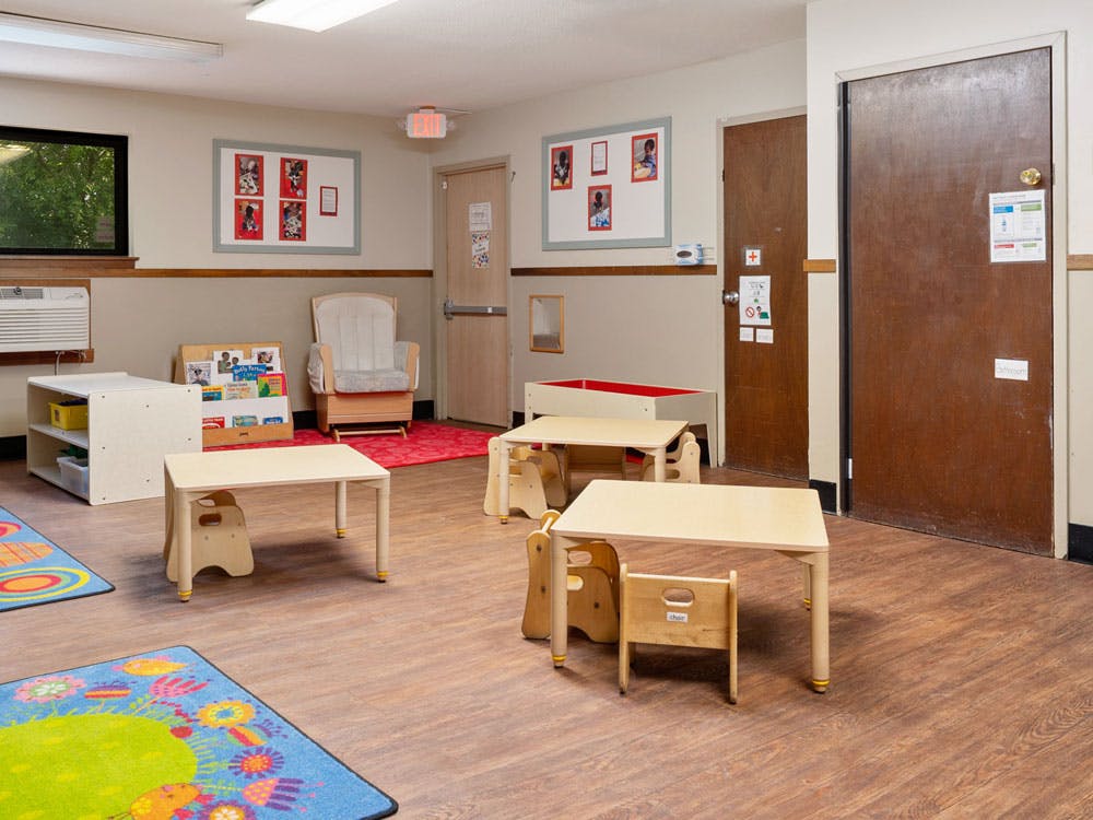 Classroom with small tables and chairs, book display, and a rocking chair
