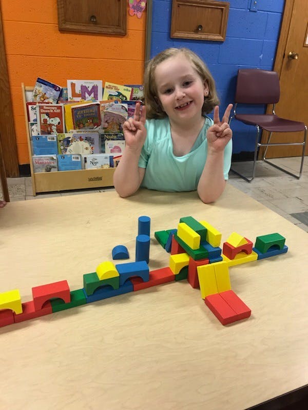 Child making peace signs with hands above a table with colorful blocks