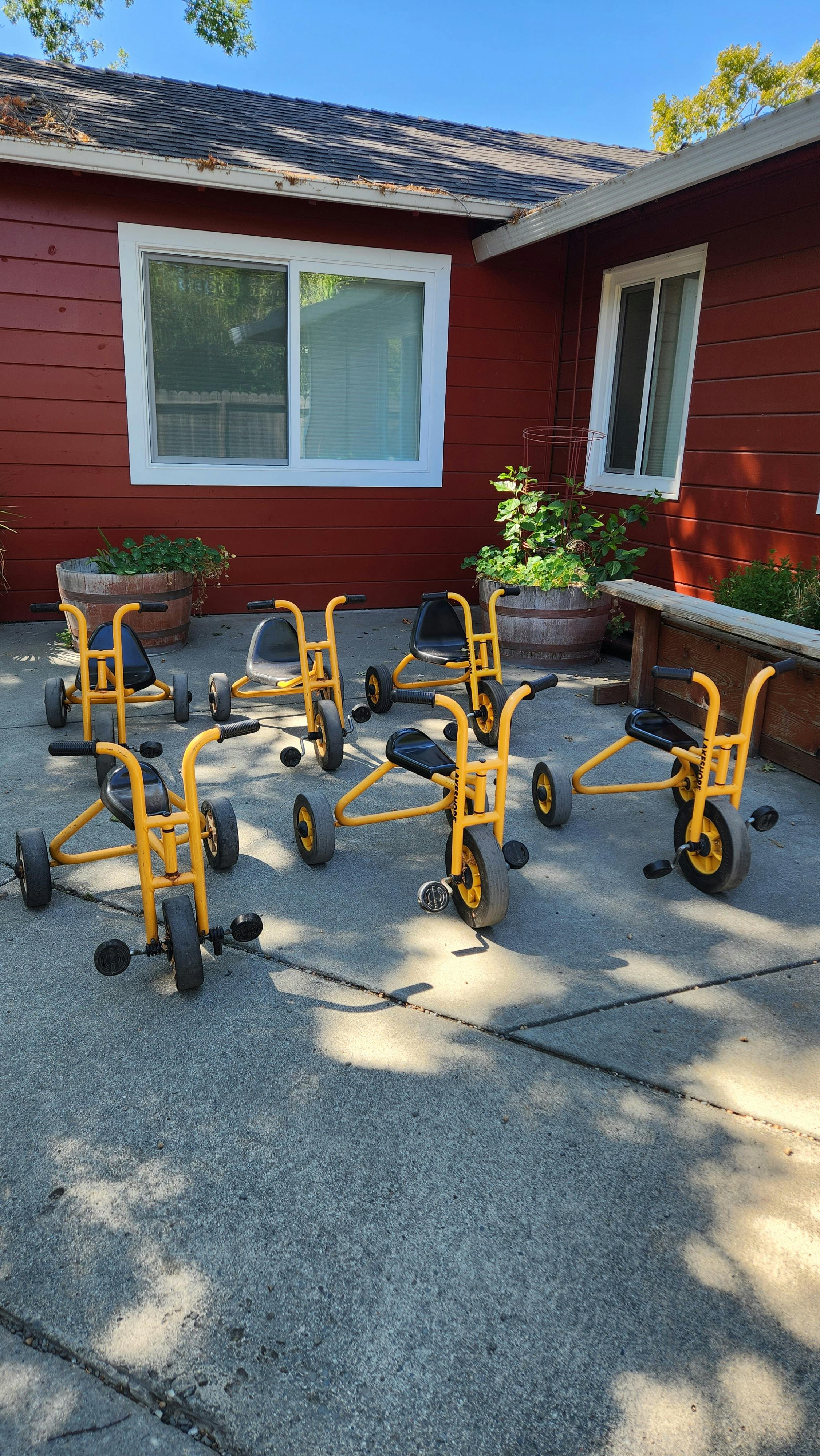 Multiple yellow tricycles on a paved surface in front of a red building