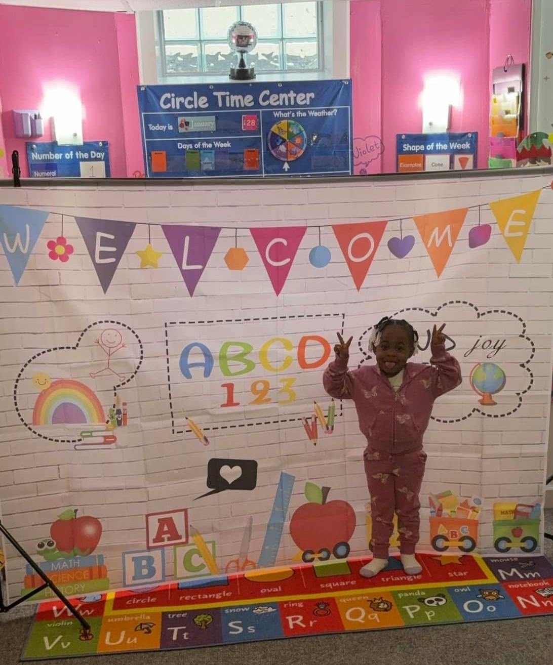 Child standing in front of a "Welcome" banner and ABC decorations