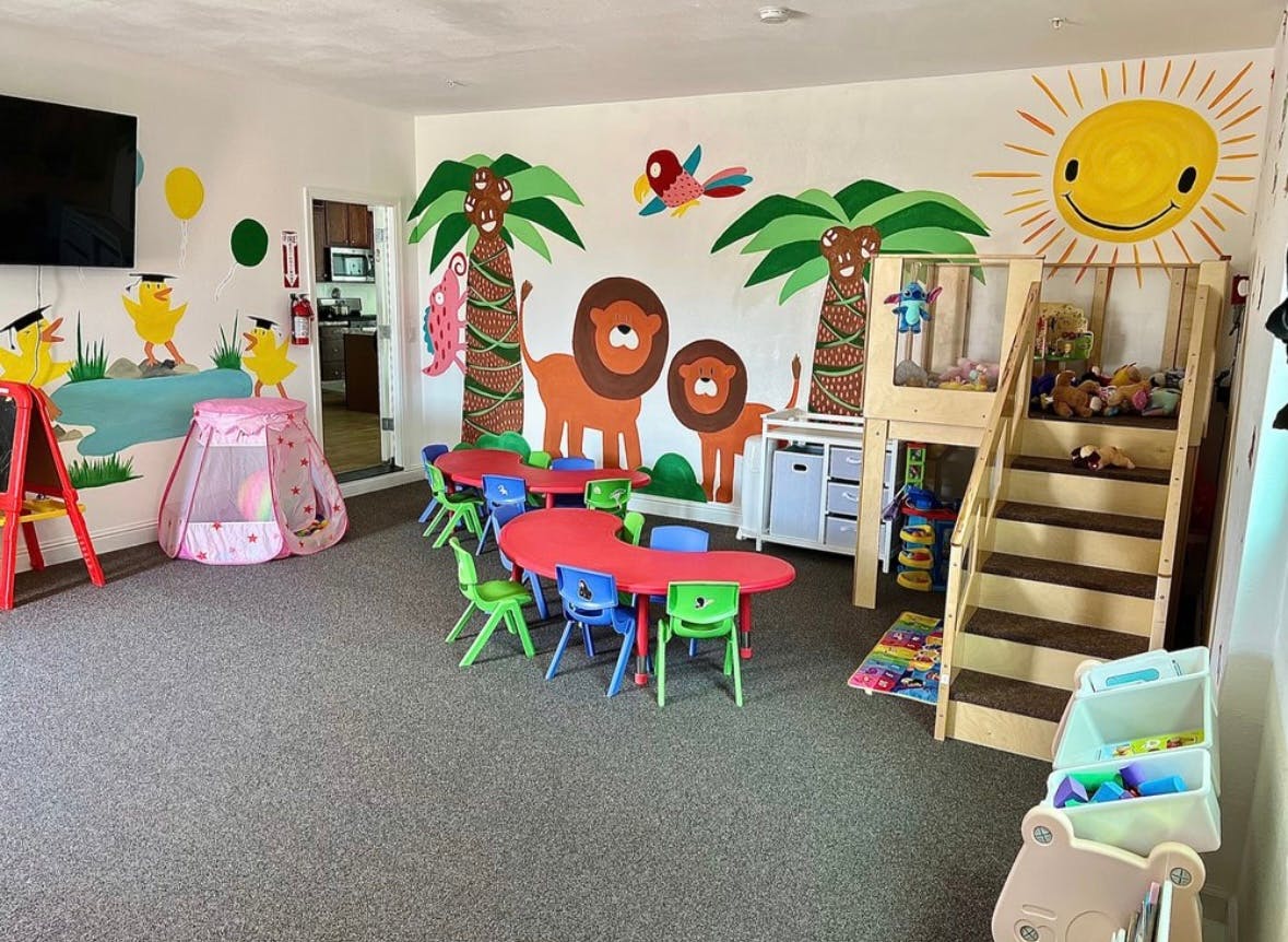 Playroom with colorful tables and chairs, jungle-themed wall murals, and a play structure