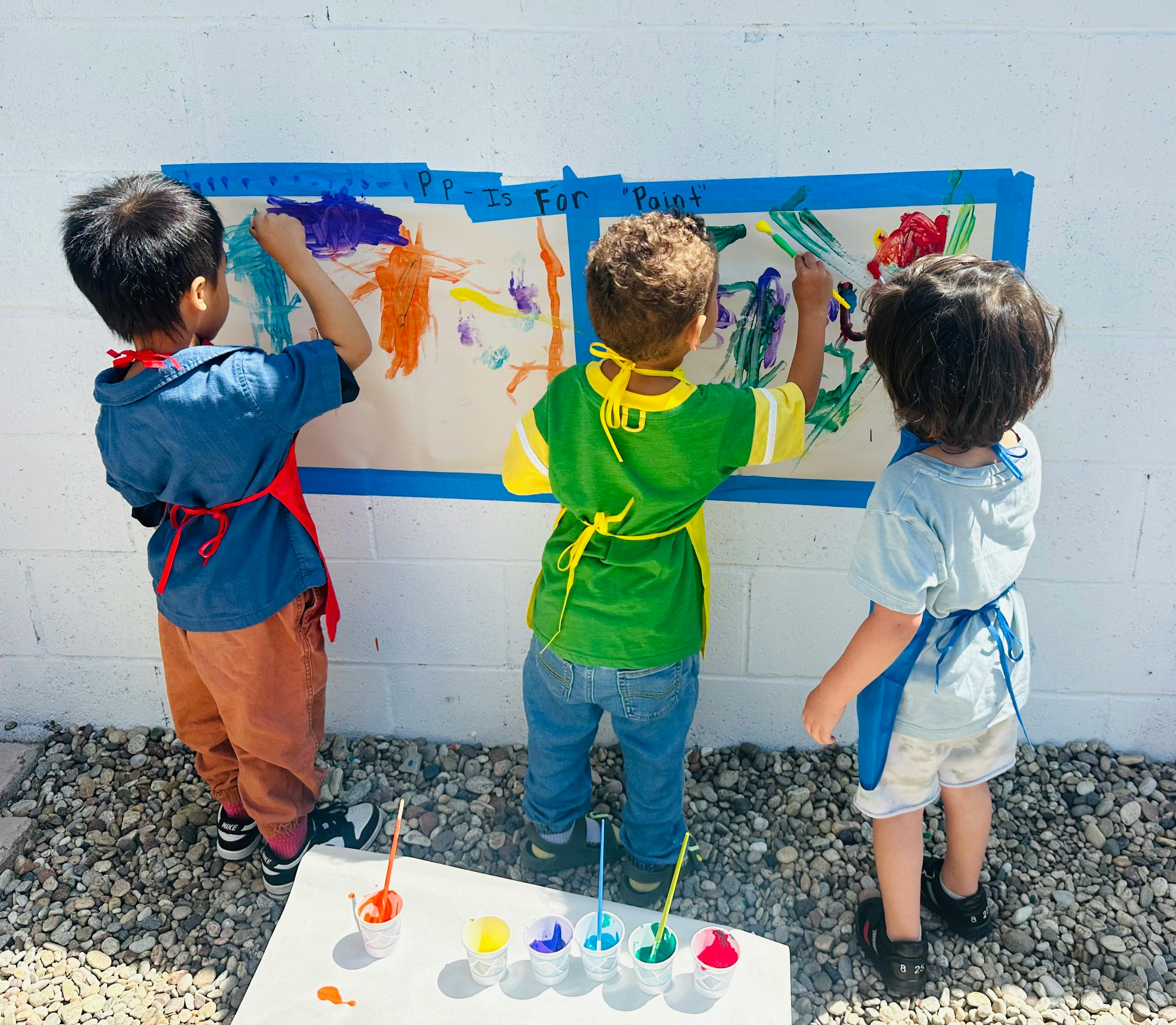 Three children painting on paper taped to a wall