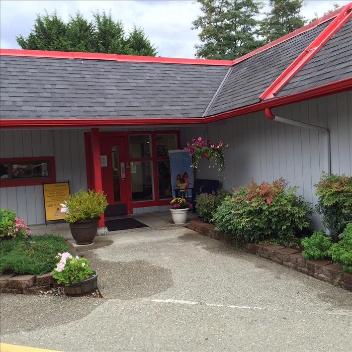 Building entrance with red door and trim, potted plants, and landscape bushes