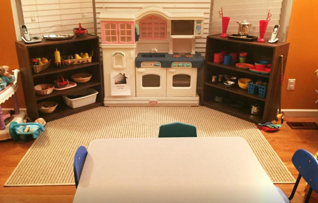 Play kitchen with shelves of toys and a table with chairs in a room