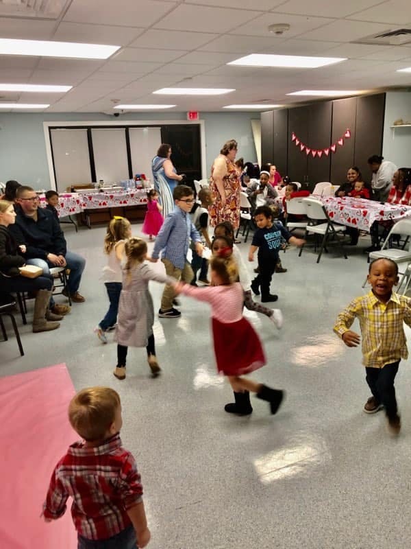 Children dancing in a room with adults seated at tables
