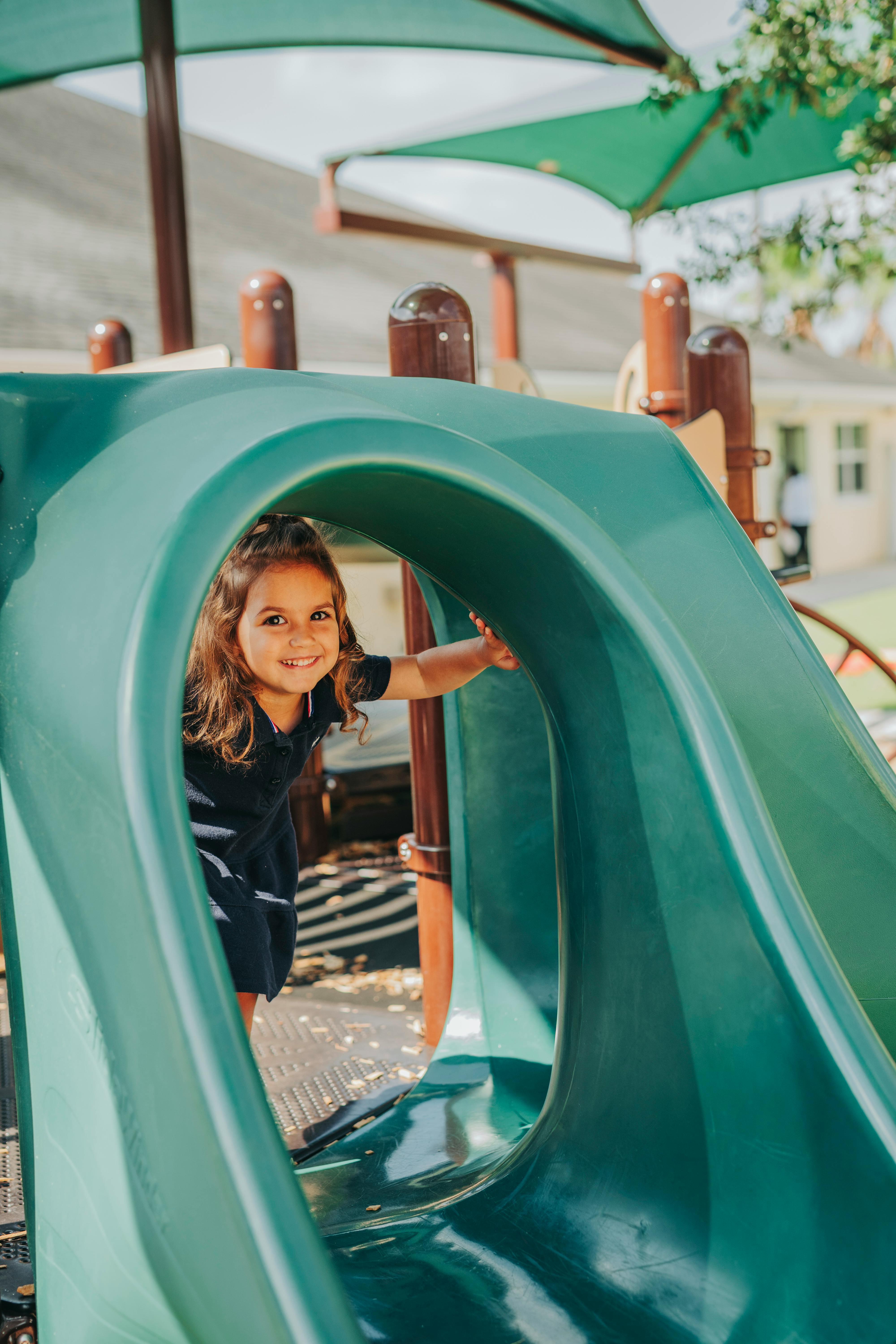 Child looking out from inside a green playground slide