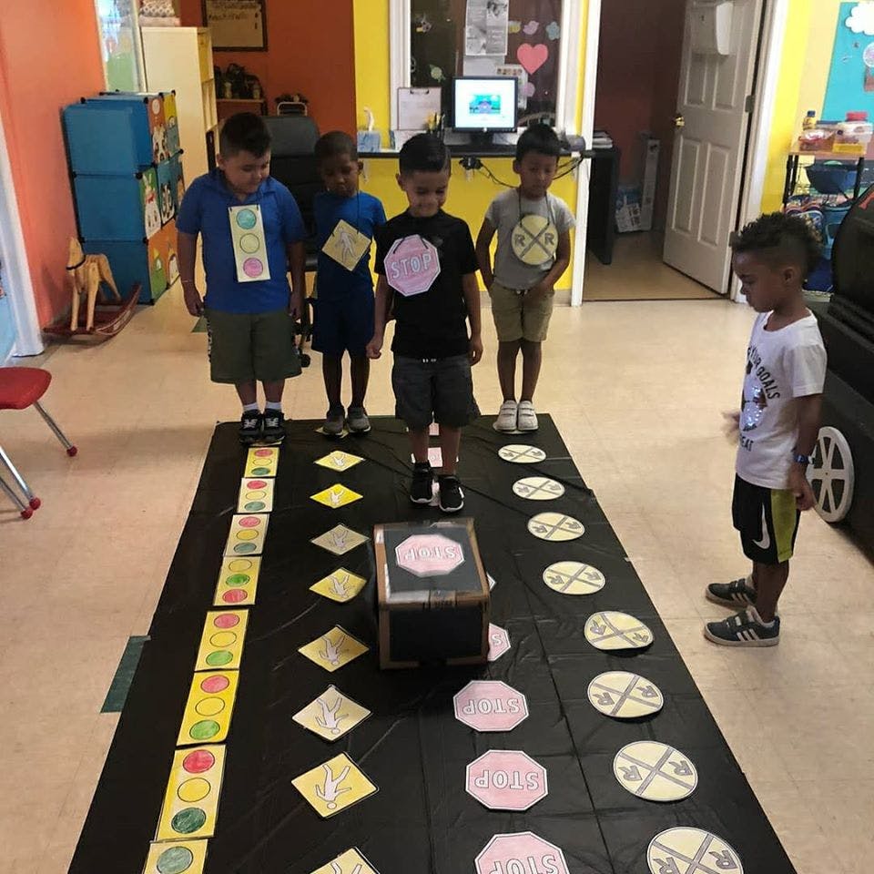 Children standing around a mat with shapes and a small robot